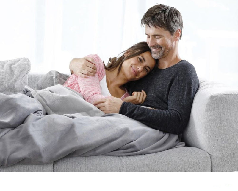 mann og kvinne på en grå sofa med et grått elektrisk varmeteppe over seg